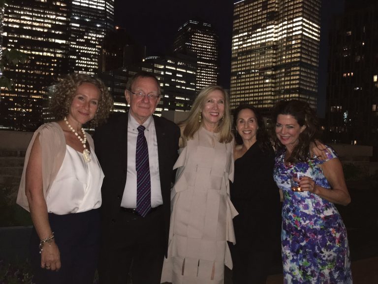 Five guests at an evening rooftop gathering against a city skyline