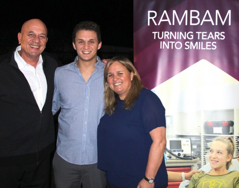 Three supporters beside a Rambam Turning Tears Into Smiles banner