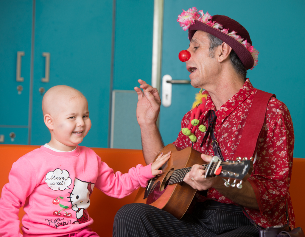 A young patient laughing with a medical clown playing guitar