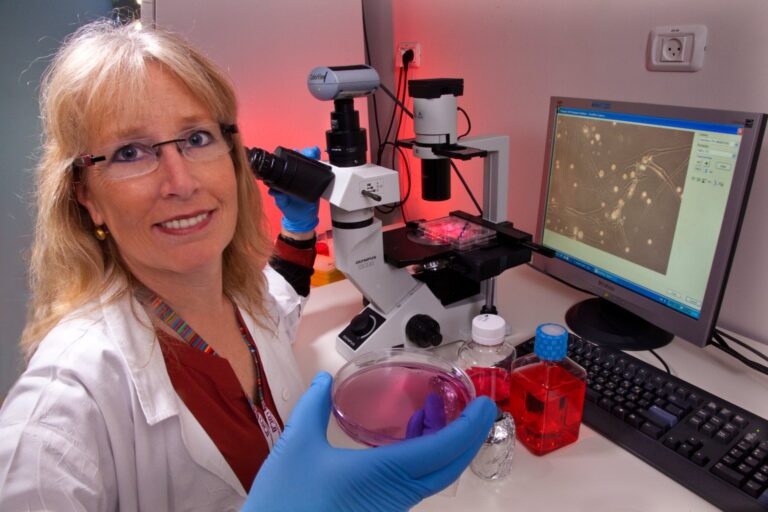 A researcher holding a culture dish beside a lab microscope